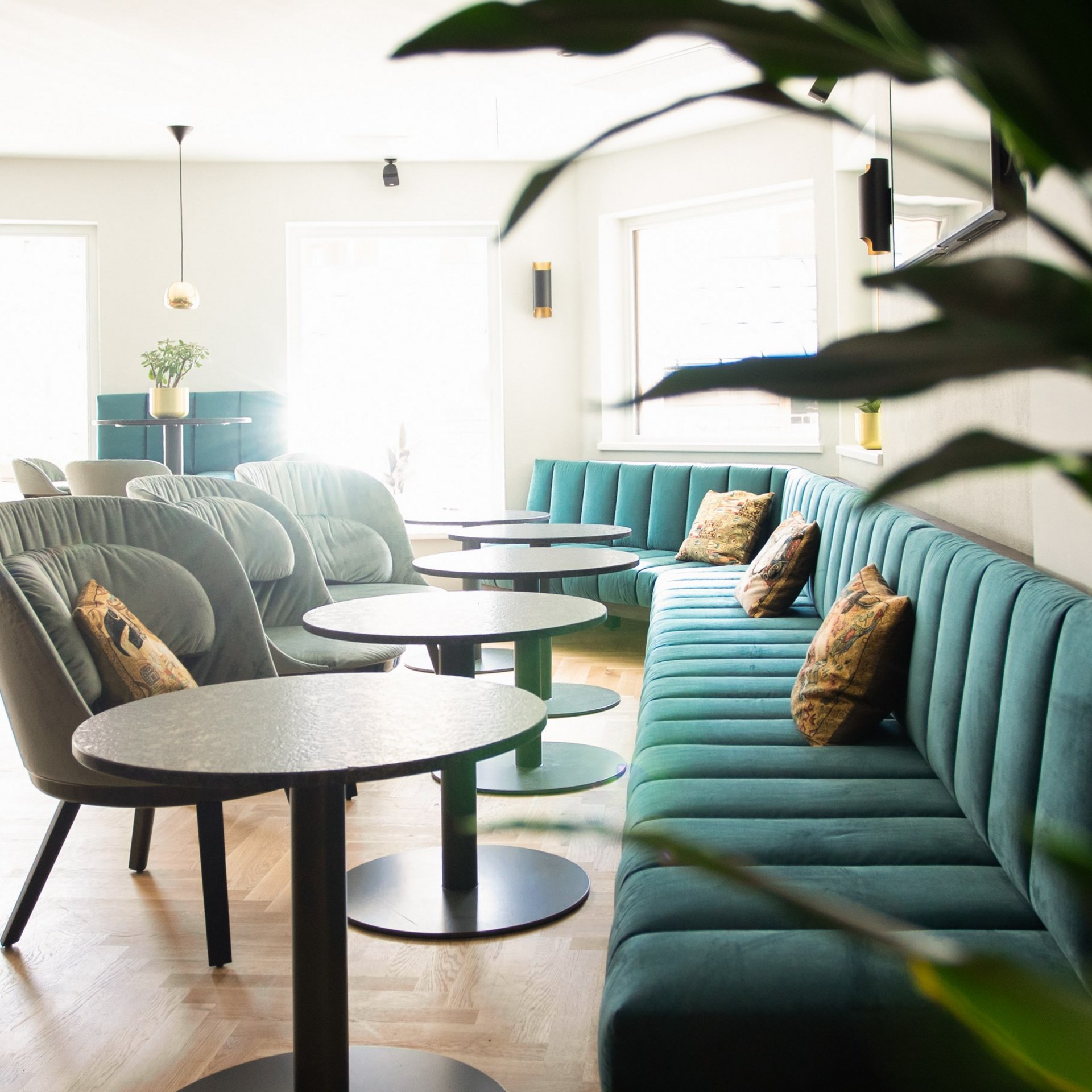 Stilvolle Lounge-Atmosphäre Elegante Lounge mit grünen Samtsofas und runden Tischen in hellem Raum.